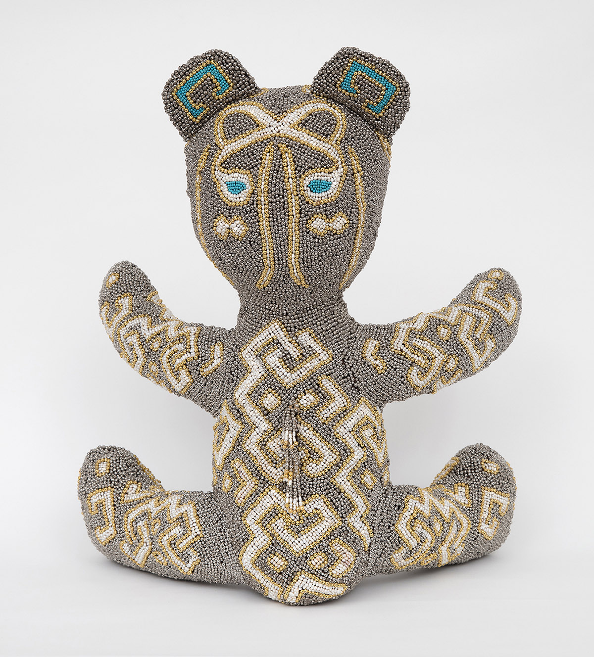 Zemi is a teddy bear made out of recycled US army uniforms. The surface of the bear is entirely covered with silver-grey zinc and gold beads, pearls and lapis lazuli stones. It was inspired by the Beaded Zemi in Rome's Pigorini Museum, one of the finest surviving examples of Taino art produced before the disappearance of this culture in 16th century. Tainos were the principal inhabitants of Puerto Rico, Cuba, Jamaica, Hispaniola and Florida before the settlement of the region by Spanish colonists. Similar to a fetish object, the Beaded Zemi represents a supernatural character with coexisting Taino, African and European features.