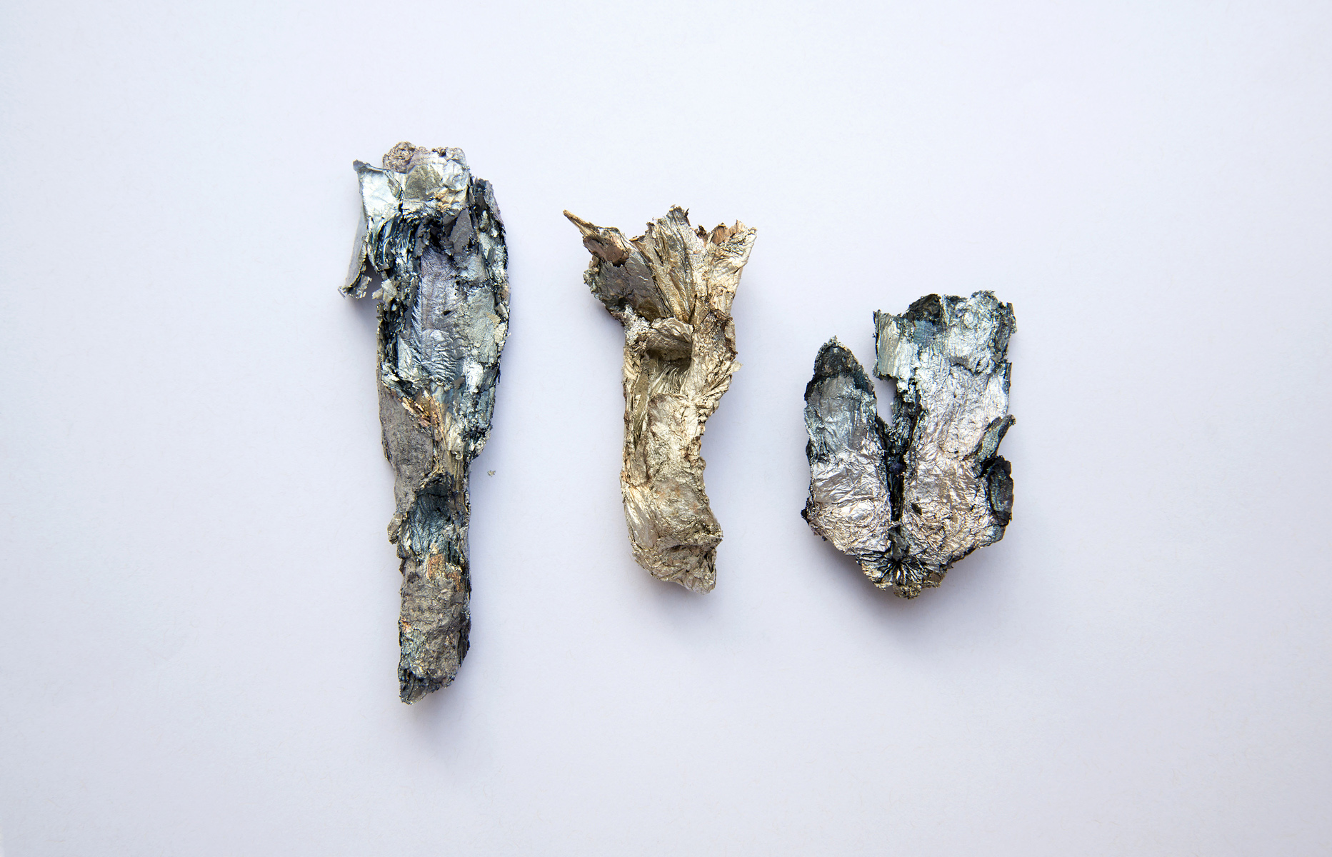Three oxidized foil sculptures sit centered on a light background.