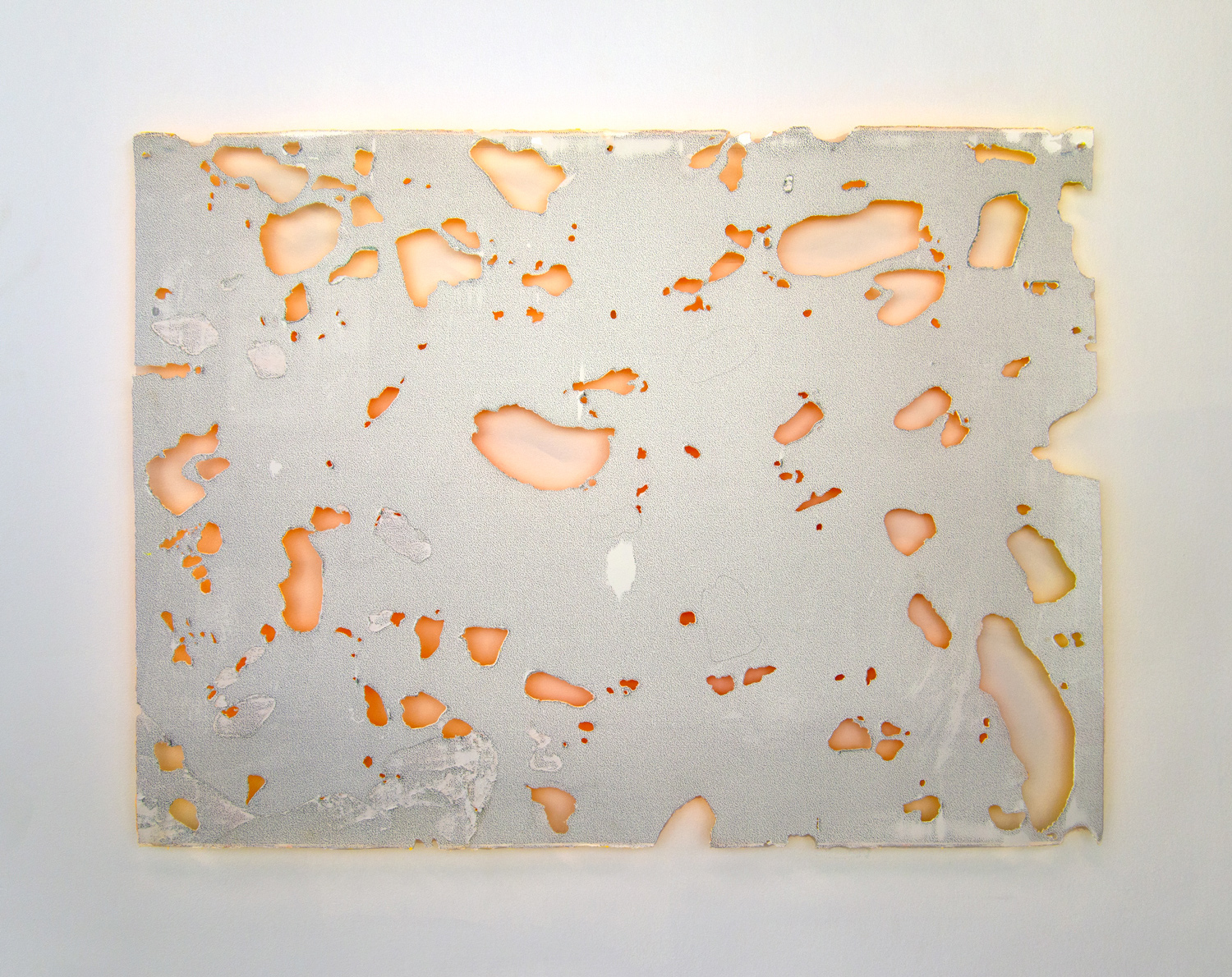 A rectangular piece of paper pierced by many irregular shaped holes floats in front of a white wall.