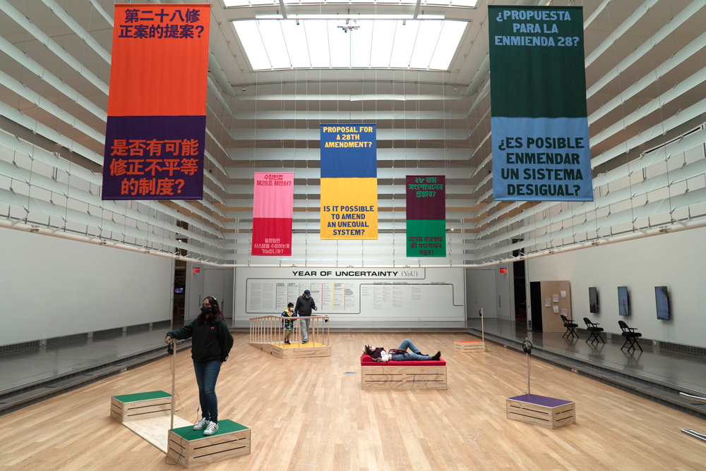 Installation at the Queen Museum featuring sonic soap box sculptures in multiple colors and designs with colorful banners above. Each banner reads “Proposal for a 28th amendment? Is it possible to amend an unequal system?” in the five most spoken languages in Corona, Queens (Simplified Chinese, Spanish, Korean, English and Bengali).