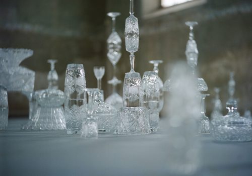 Crystal glass is known for its fragility. By layering crystal glass objects I multiply the feeling of fragility. Individual crystal glass objects are not glued together and as such may break by simple sound waves produced by passer-by.