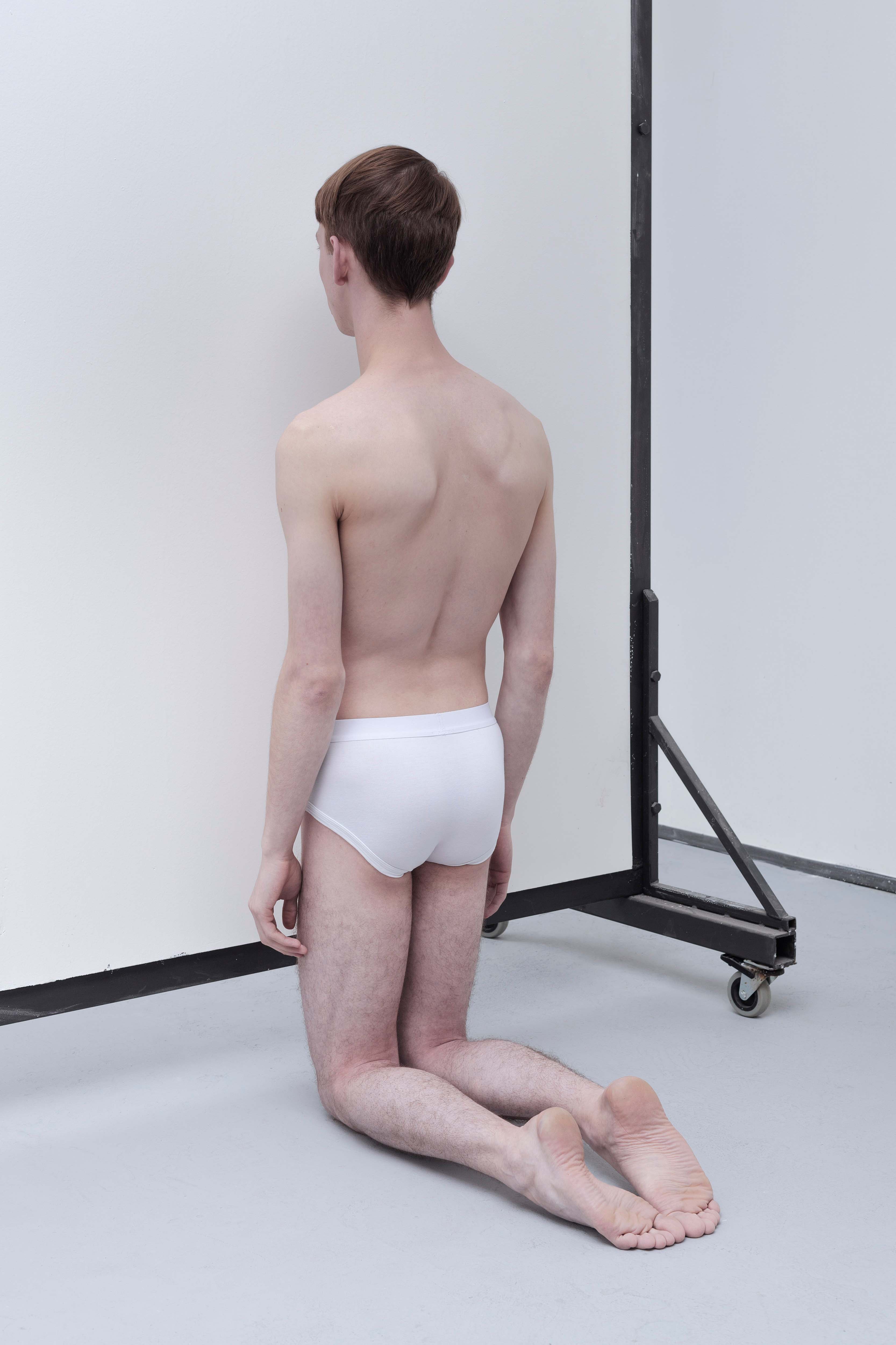 The exhibition project brings performance and installation together. A semi-naked young man kneels against the wall motionless. The viewer does not see his face; he remains anonymous. It is not clear whether he is praying or whether it is an act of punishment.