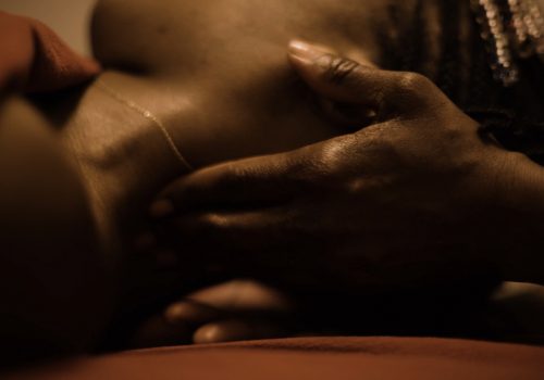 A close up image of the artist receiving massage therapy. Her neck is being massaged by the hands of the therapist and her face is out of view, head tilted away from the camera.