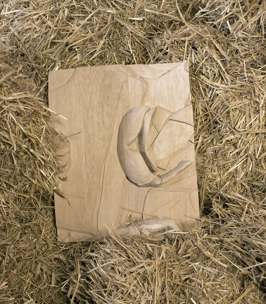 A relief showing safety goggles, a base cap and a safety west lies in a pile of straw.