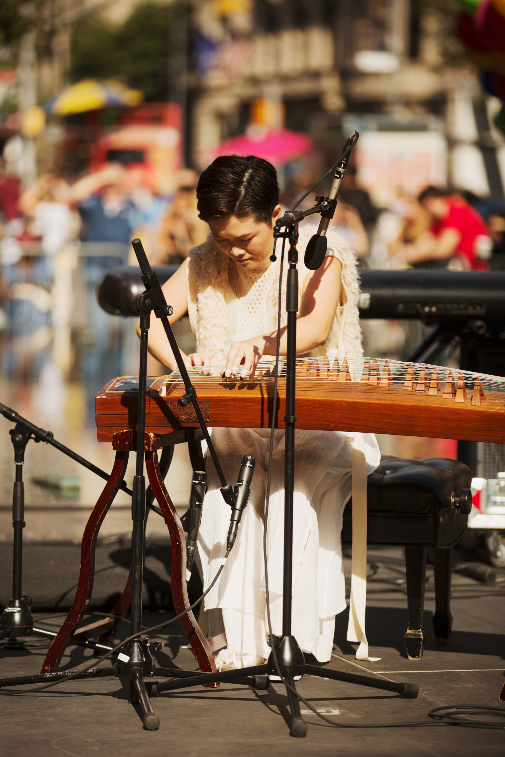 Clae Lu performing on the guzheng (Chinese zither) with a large audience at the Metropolitan Museum of Art.