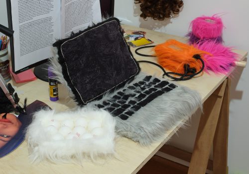 A messy desk with a laptop, hard drives, and duct tape made of faux fur