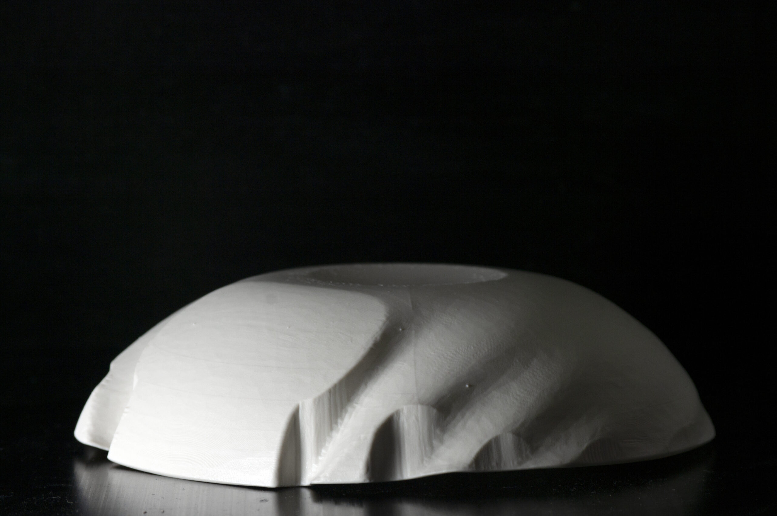 This is a photo of a delicate white porcelain bowl sitting upside down on a shiny black surface. The background is black.