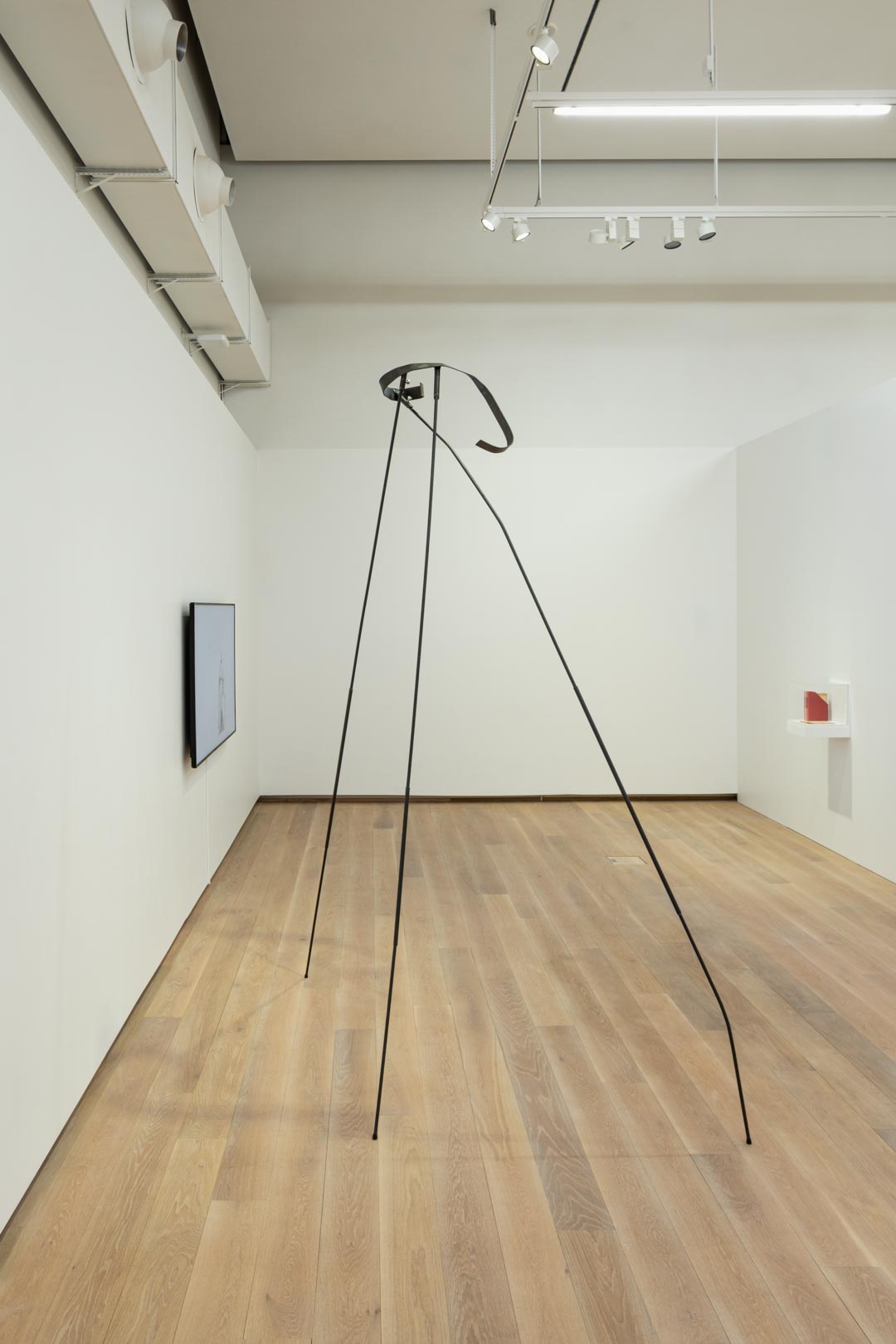 Tall steel sculpture with long legs, in a white exhibition room.