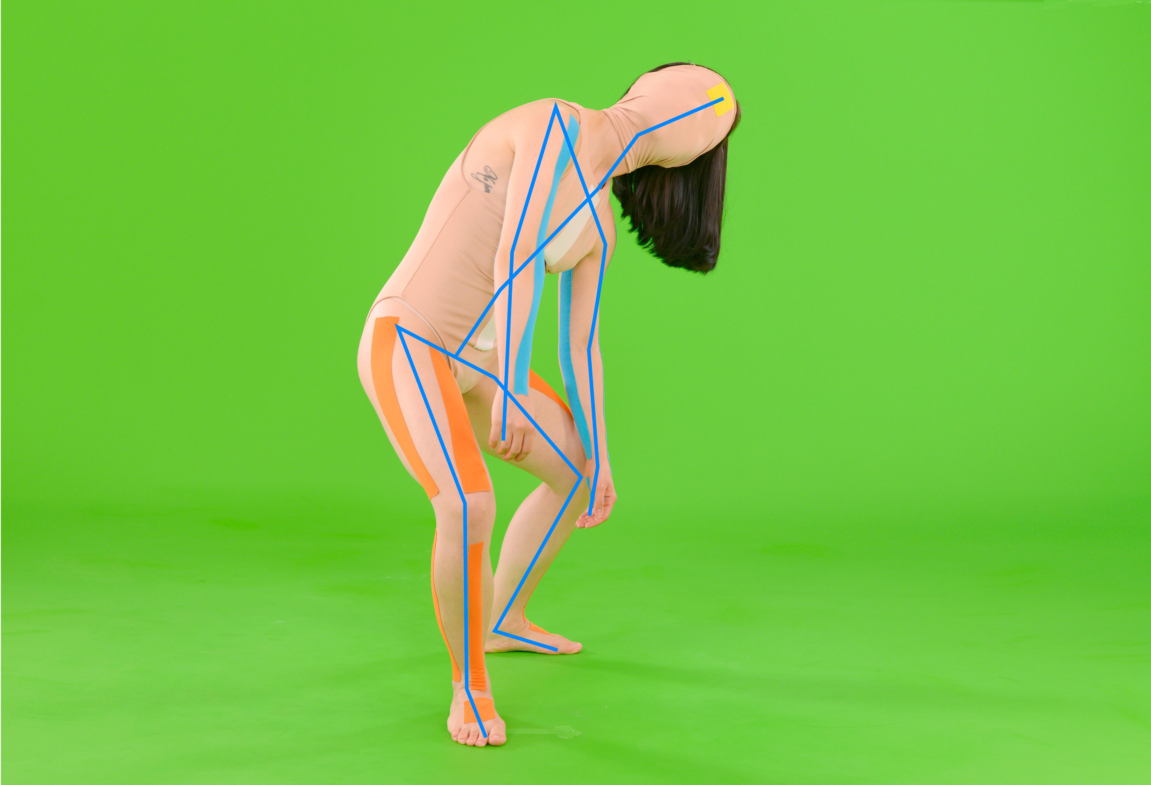 Half human, half machine, the figure of the video installation Infinite Posture Dataset is stuck within the confinements of the screen and either following or giving certain instructions to the rhythm of the machine. She is wearing a tight suit reminiscent of the ones used for motion capture techniques, involving the digital registration of body movement. In the work the performer is talking about the feelings stirred in her body memory while performing the movements and which results in spoken out loud, incoherent emotions. Her limbs also seem to have been detached. All in all, the spectator is left with random pieces of the puzzle. In similar cases we would usually focus on the face, but that too is hidden. While observing the deconstructed and reformulated poses of the performer, could the machine perhaps understand what she is trying to communicate? Vogelaar reveals how the bigger picture continues to be intangible to both human and machine. Neither human, nor machine has all the answers.