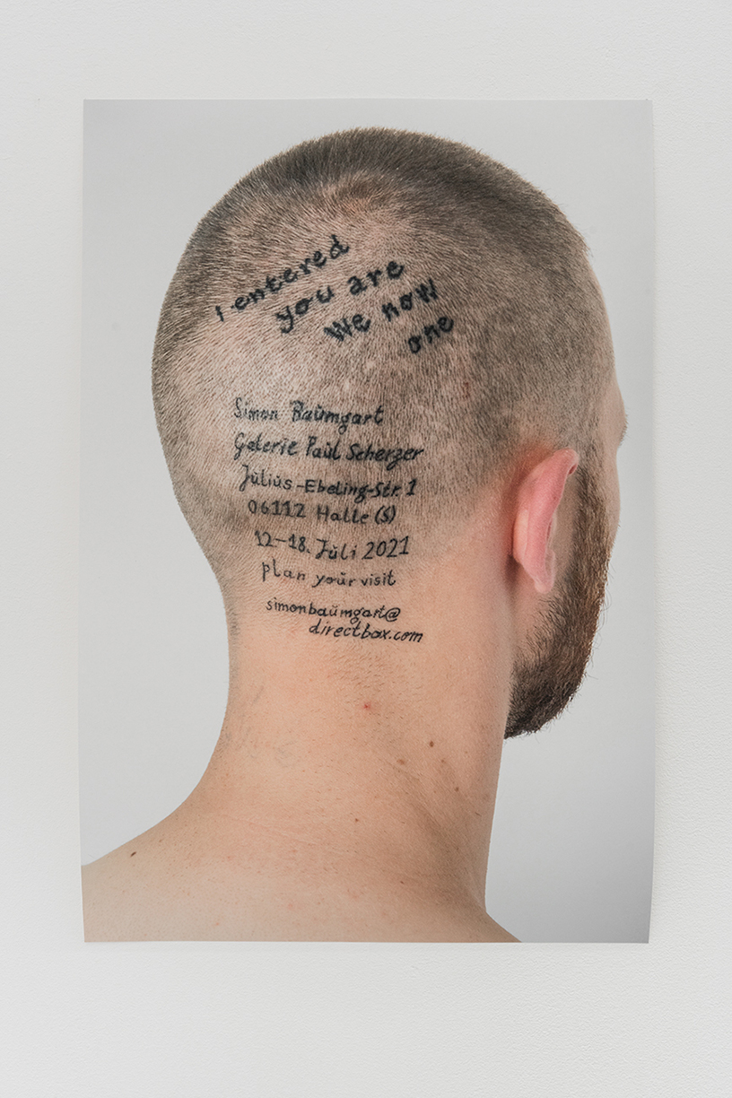 The back of the artist's head serves as an exhibition poster with tattooed dates of his show 