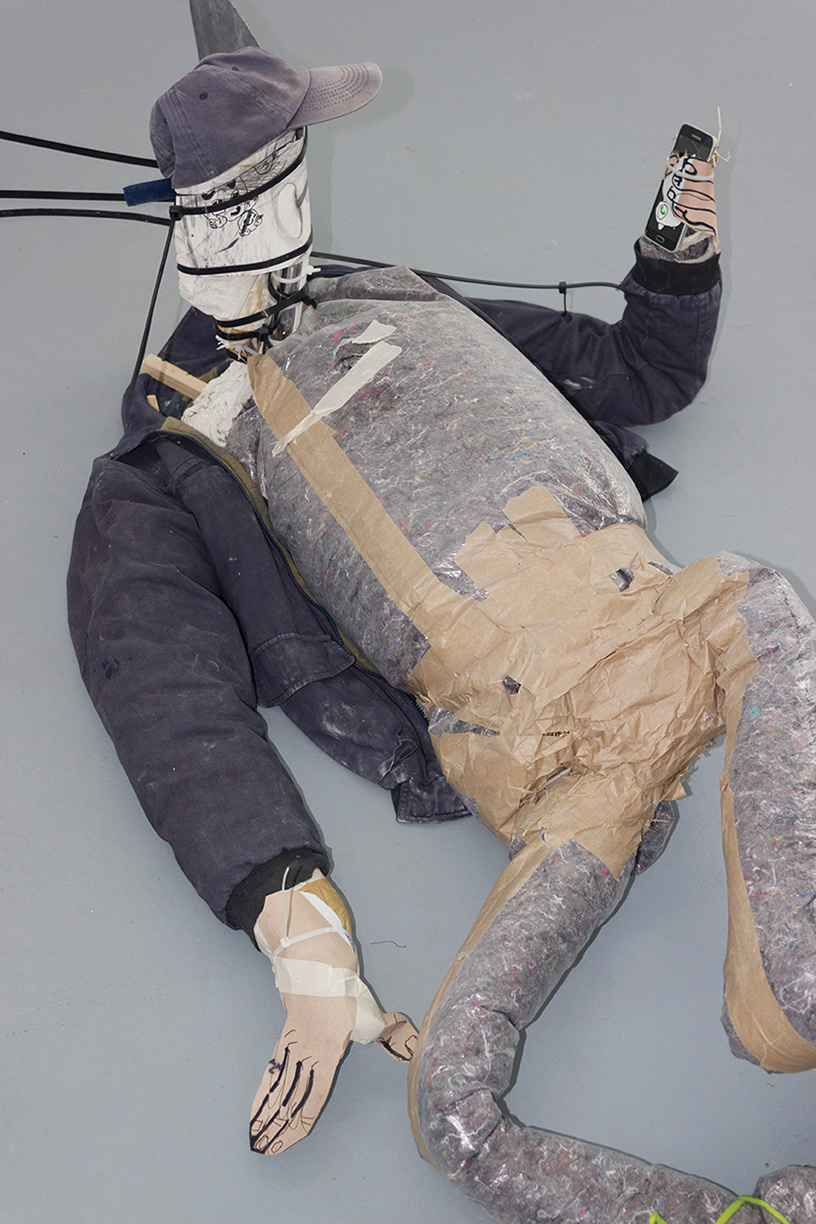 Figurative sculpture made of stuffed clothing lying on the floor and staring at a ringing smartphone in its hand