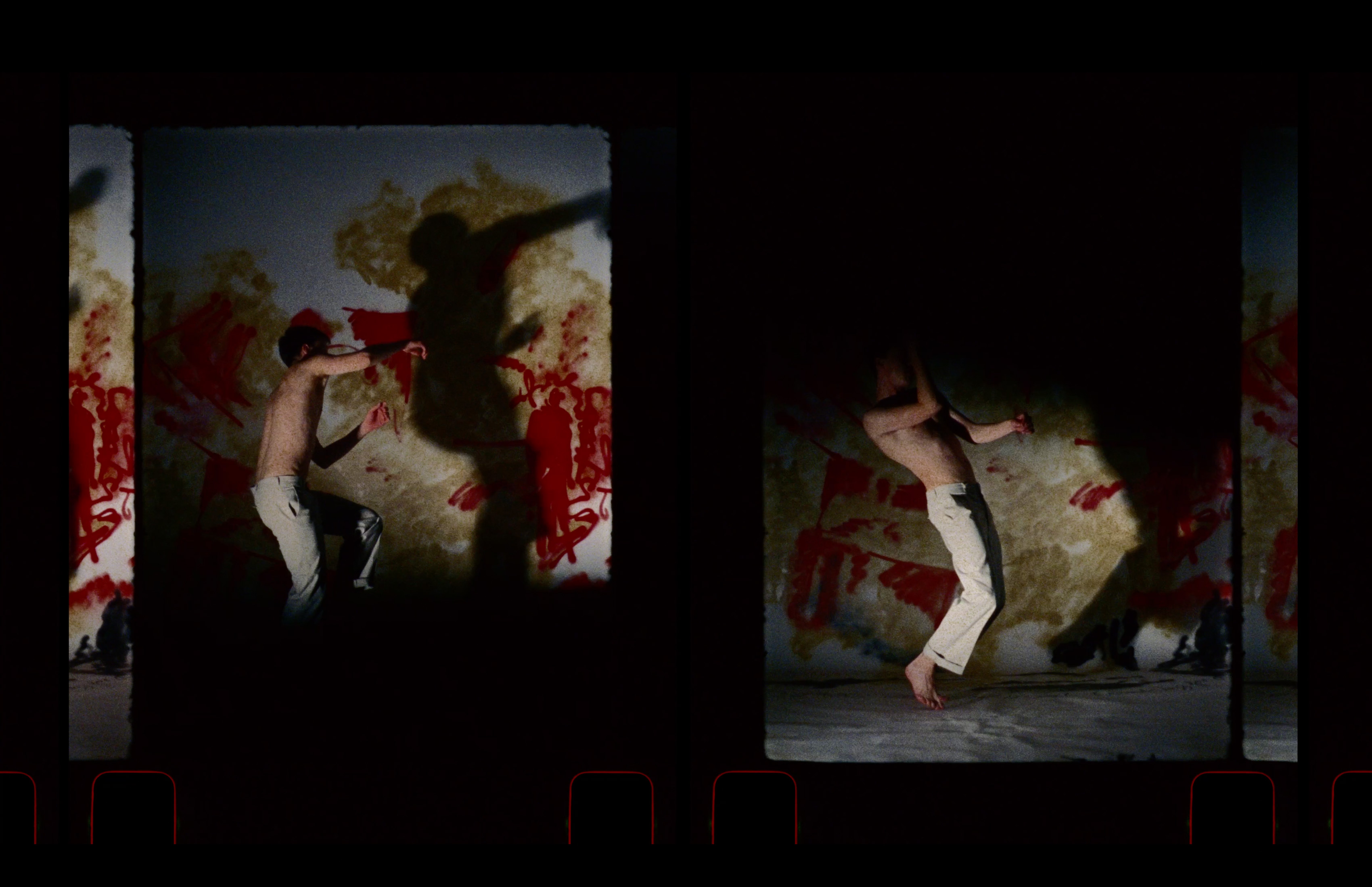 A still from 16mm film showing a male figure moving in front of a spray painted red backdrop