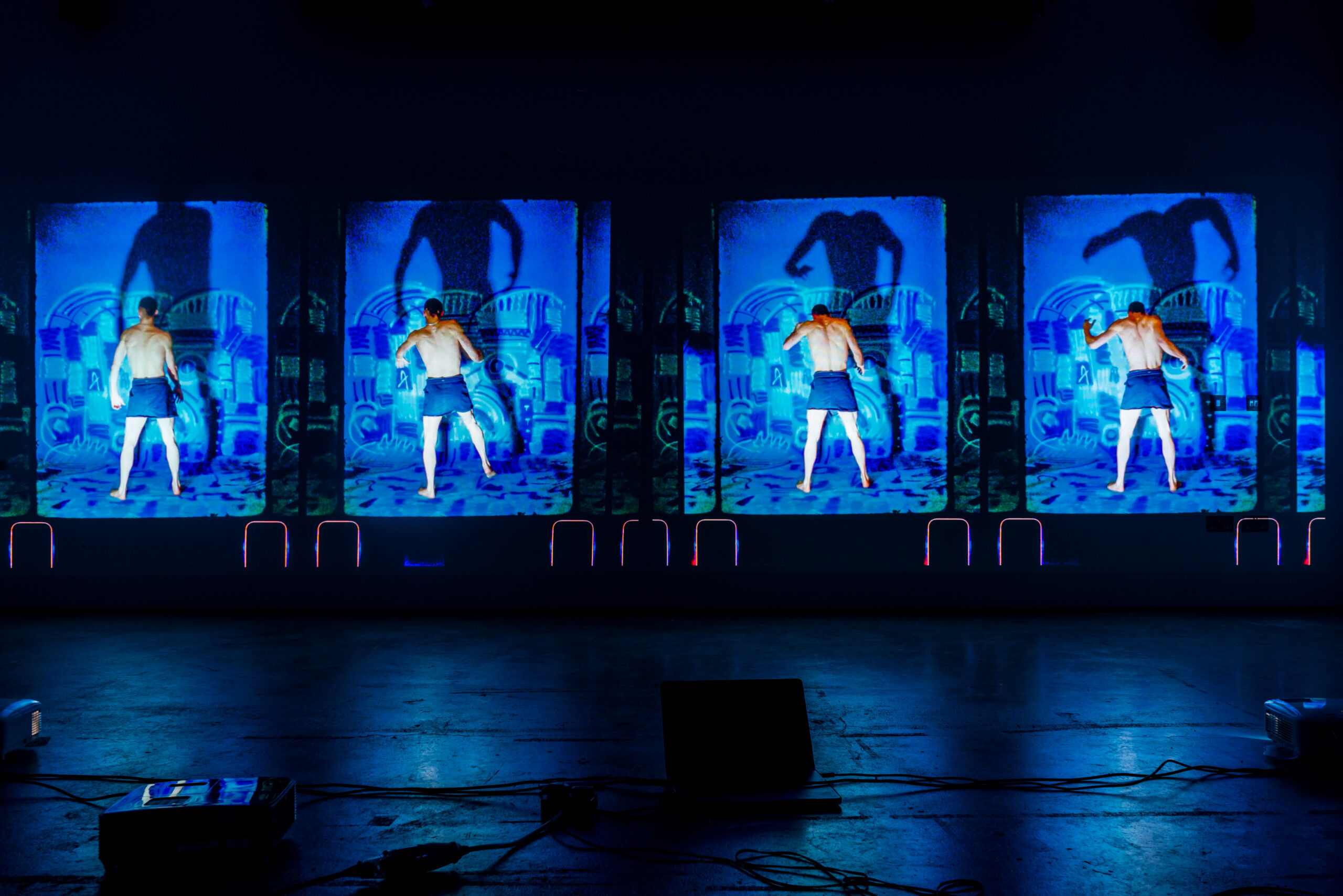 A film projection showing a man dancing with a looming shadow on the wall behind him