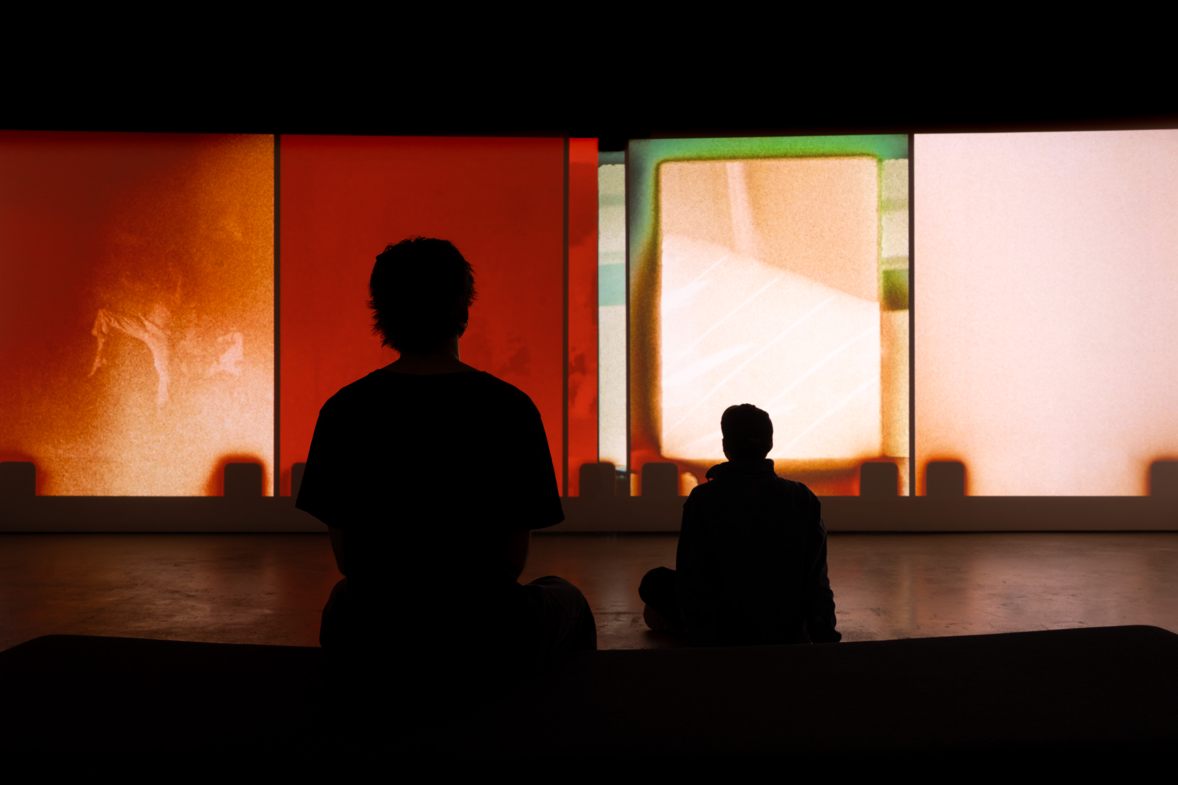 Two figures watching a colourful film projection installation