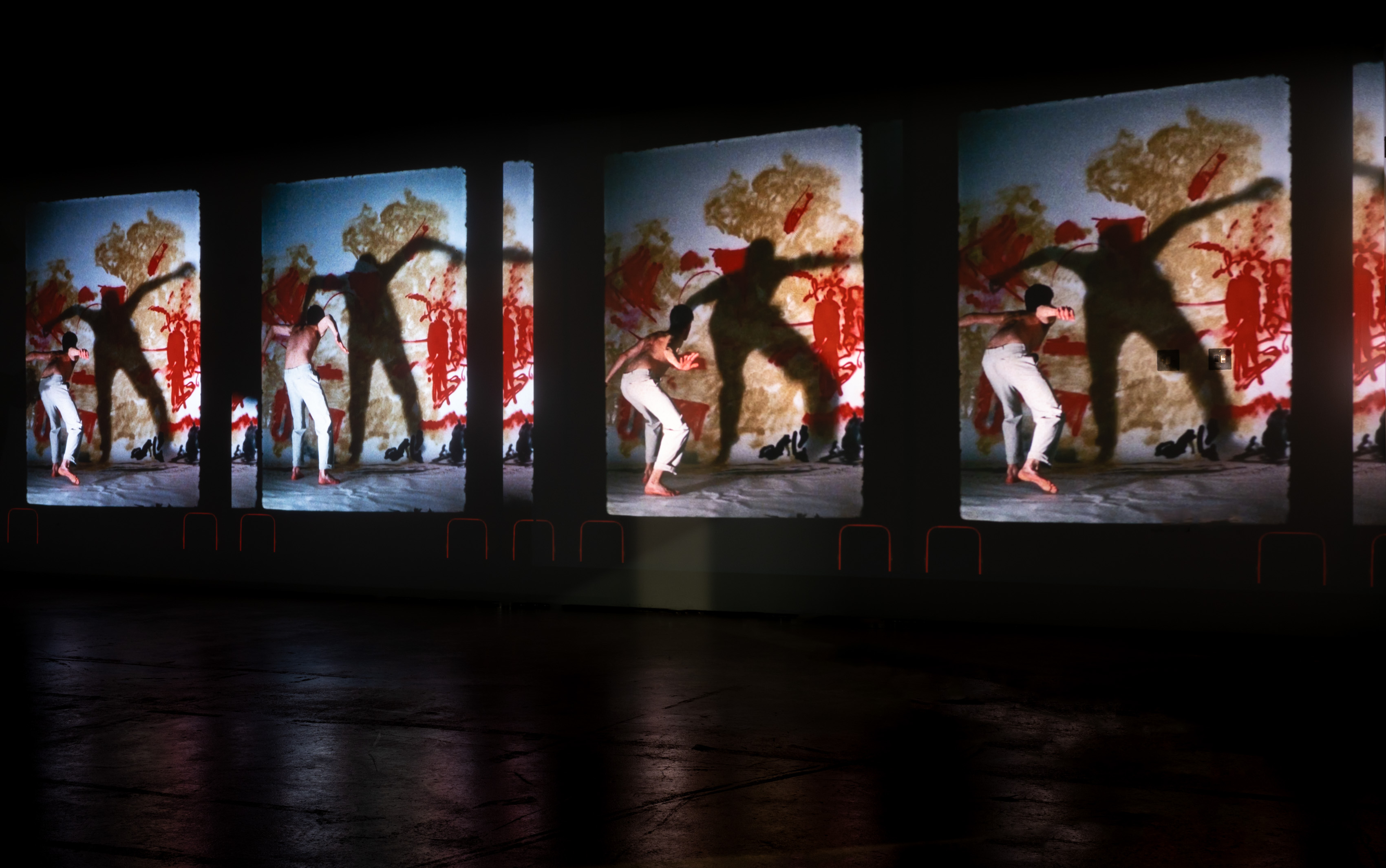 A large film projection installation consisting of 4 images of man dancing in different positions with a large shadow on the wall behind him
