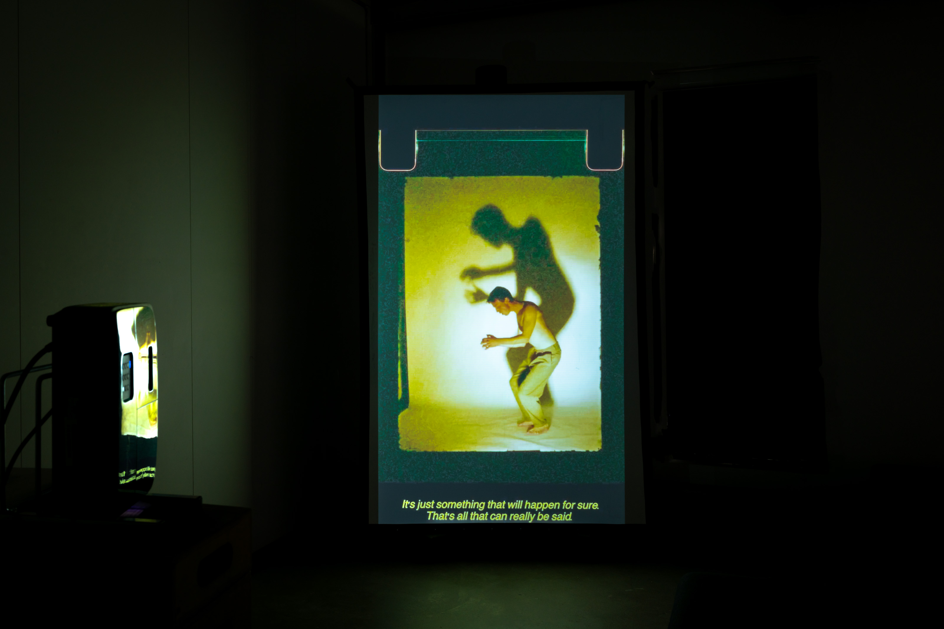 A film projection showing a man dancing with a looming shadow on the wall behind him