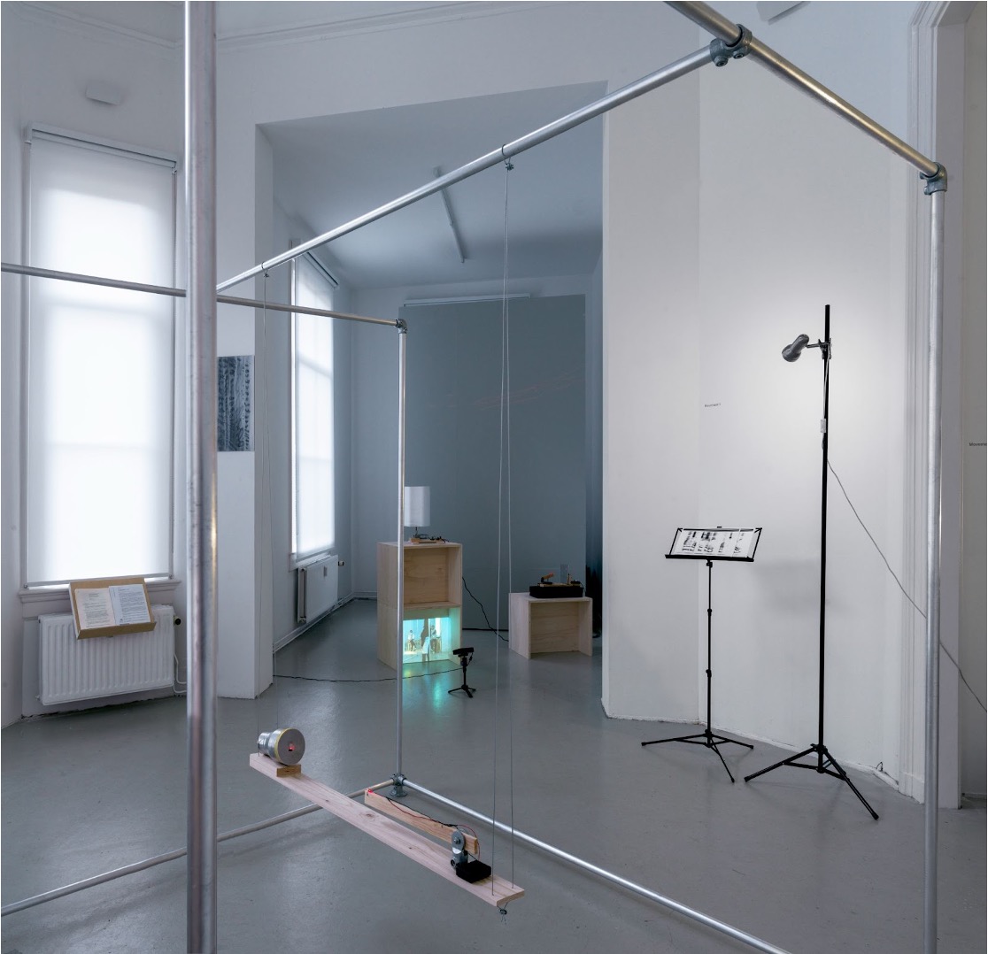 The installation view of two sound-image converts devices and spectrograms for performance. Of those two devices, one is made of a mirror, vibration speaker and laser light and the other is made of a metal cup with a rubber lid and laser lights combined on a flat wooden stick which is hung like a swing.