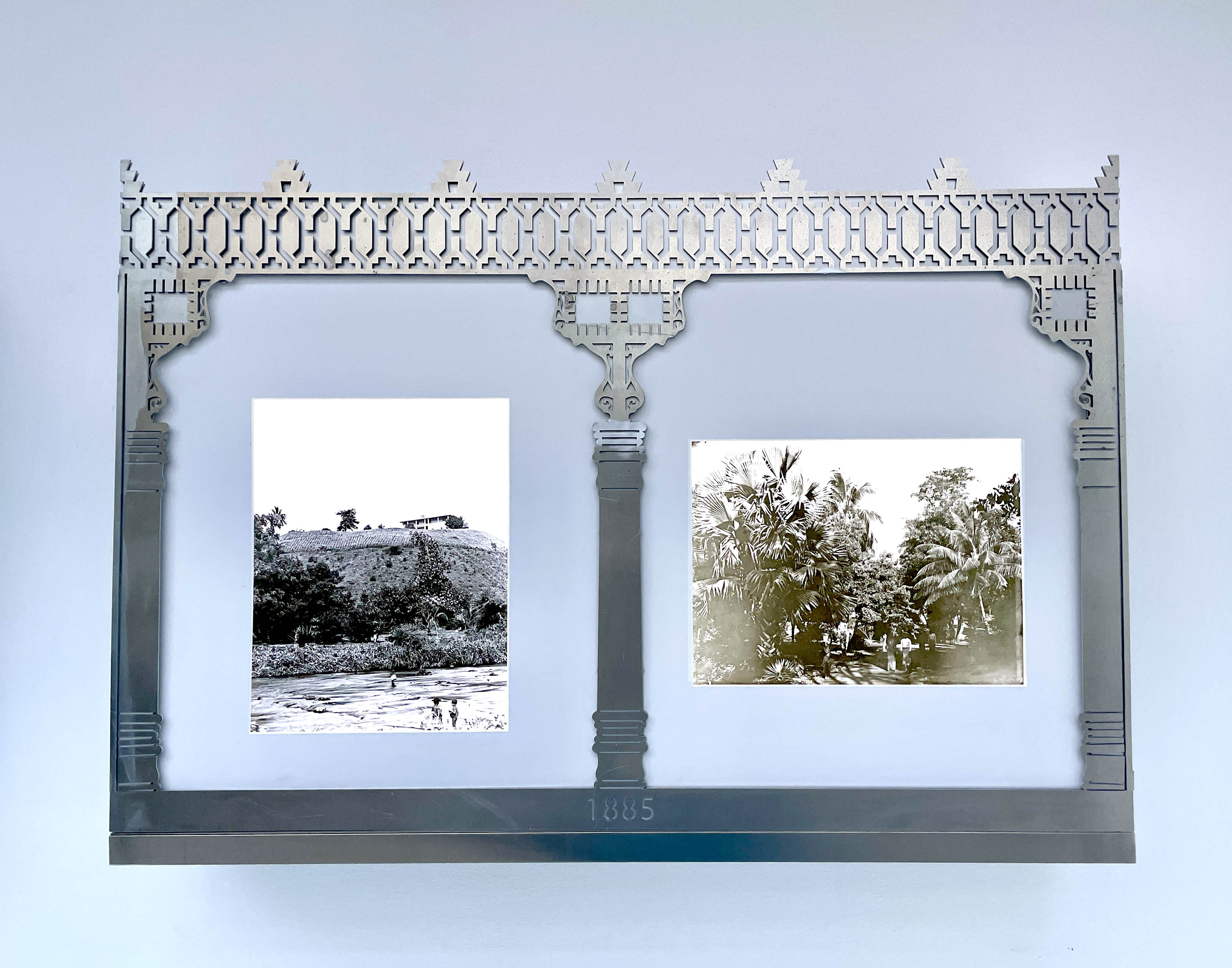 An decorative, laser-cut aluminum frame sits in front of two black and white, back-lit archival images of plants. The archival images show the Limbe Botanical Garden in Cameroon in the early 20th century.