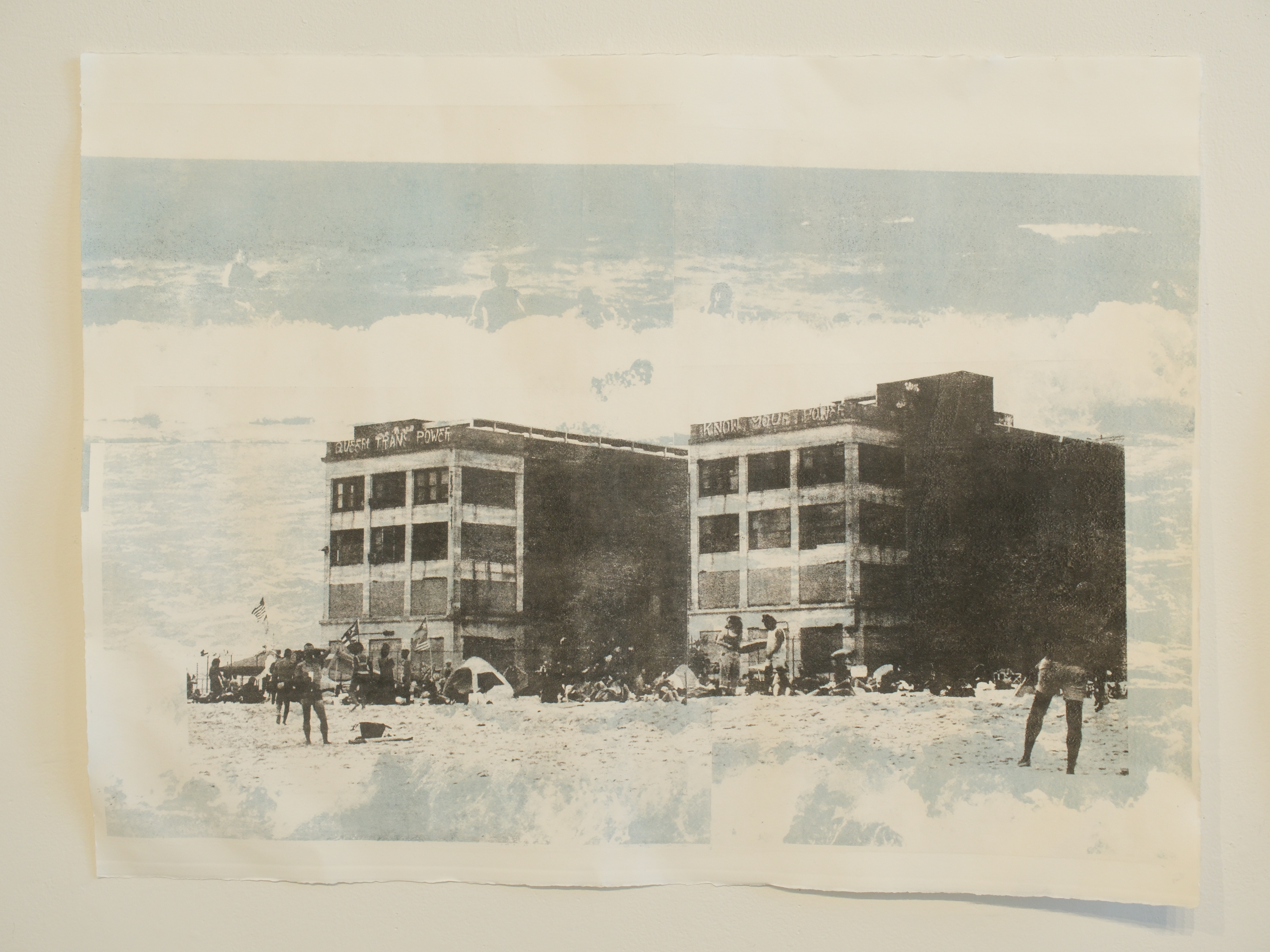 Beach goers below an abandoned graffiti covered buildings in black ink layered with people playing in ocean surf in blue-grey