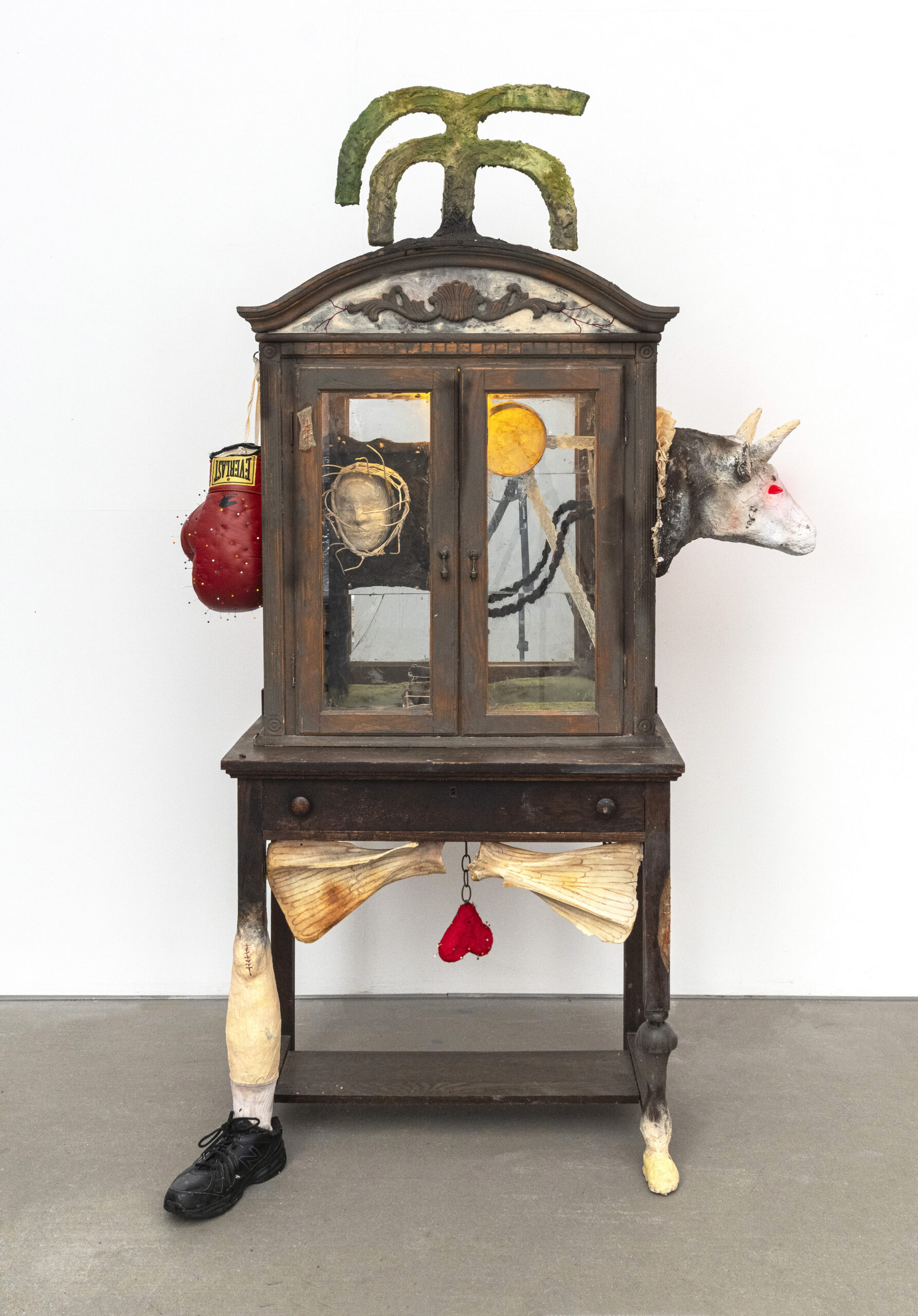 A sculpture made from a China cabinet with found objects and sculptural additions, including boxing gloves and a bull's head.