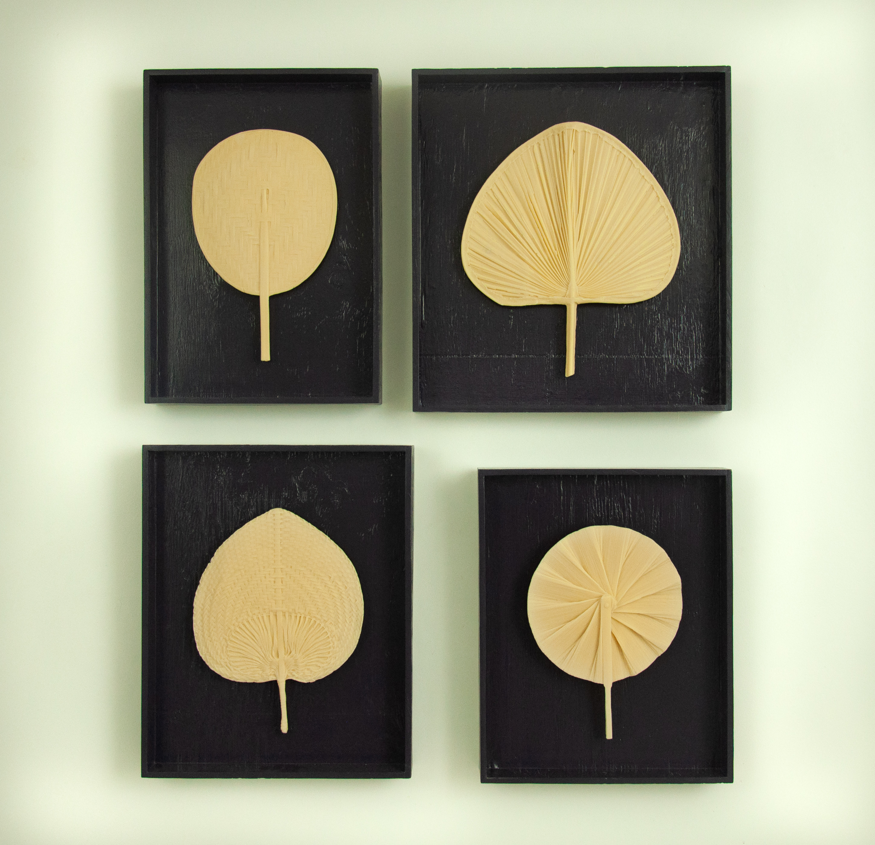 Four orange-colored hand-held fans cast in papaya soap mounted on the wall, and in dark blue open frames.