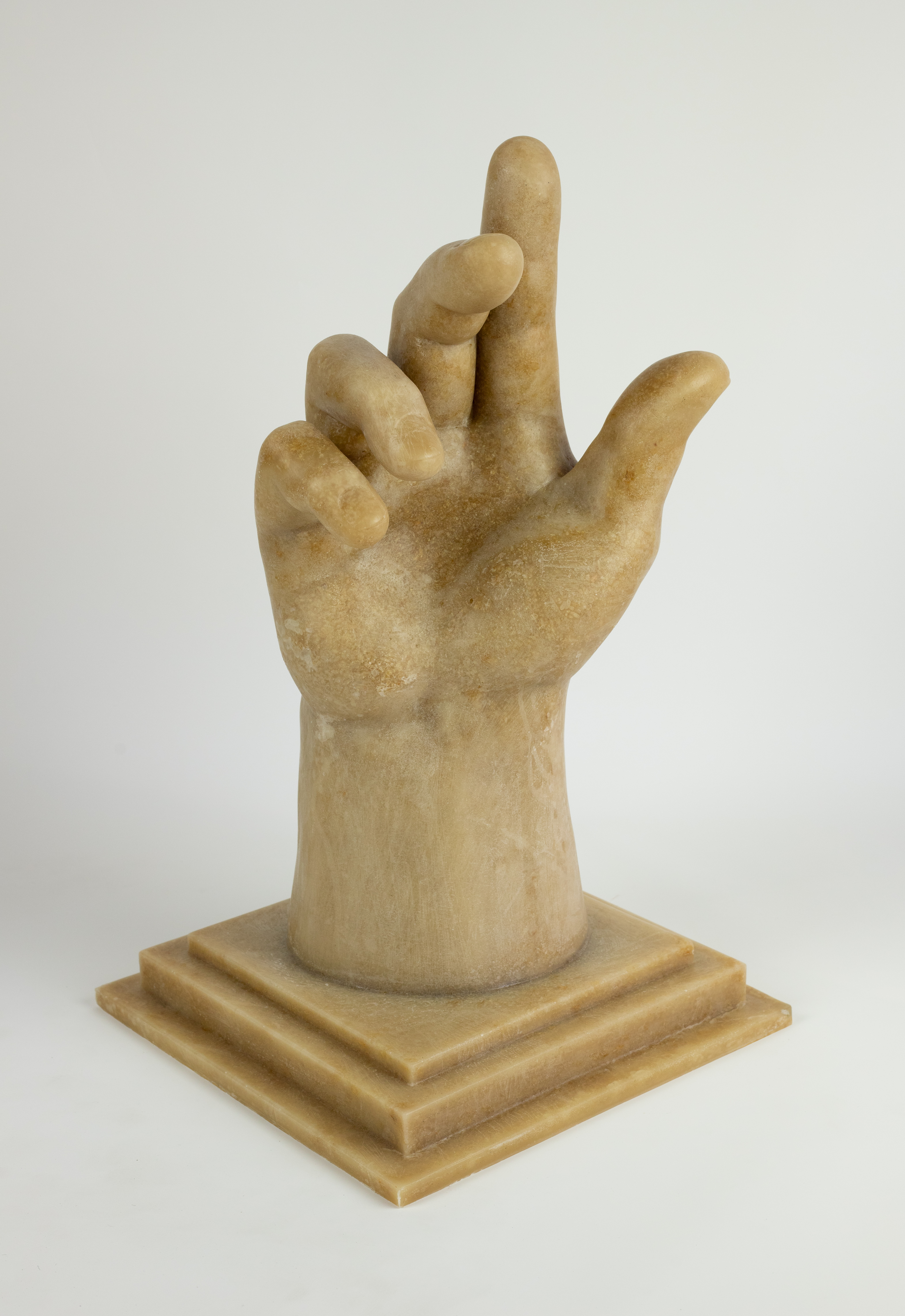 A brown colored sculpted hand with a square base posed in a slightly opened gesture with the index finger pointing up.