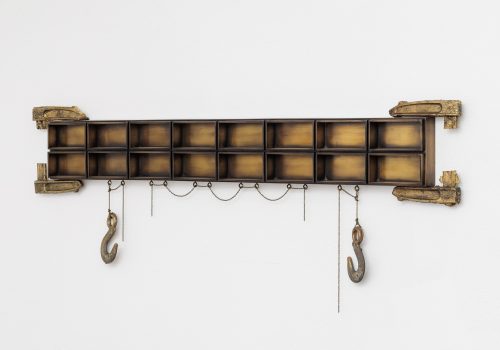 A wall-hanging sculpture made up of two long rows of brass boxes. Cast brass clamps grip the sculpture on the top and bottom. Cast brass hooks hang from the bottom.