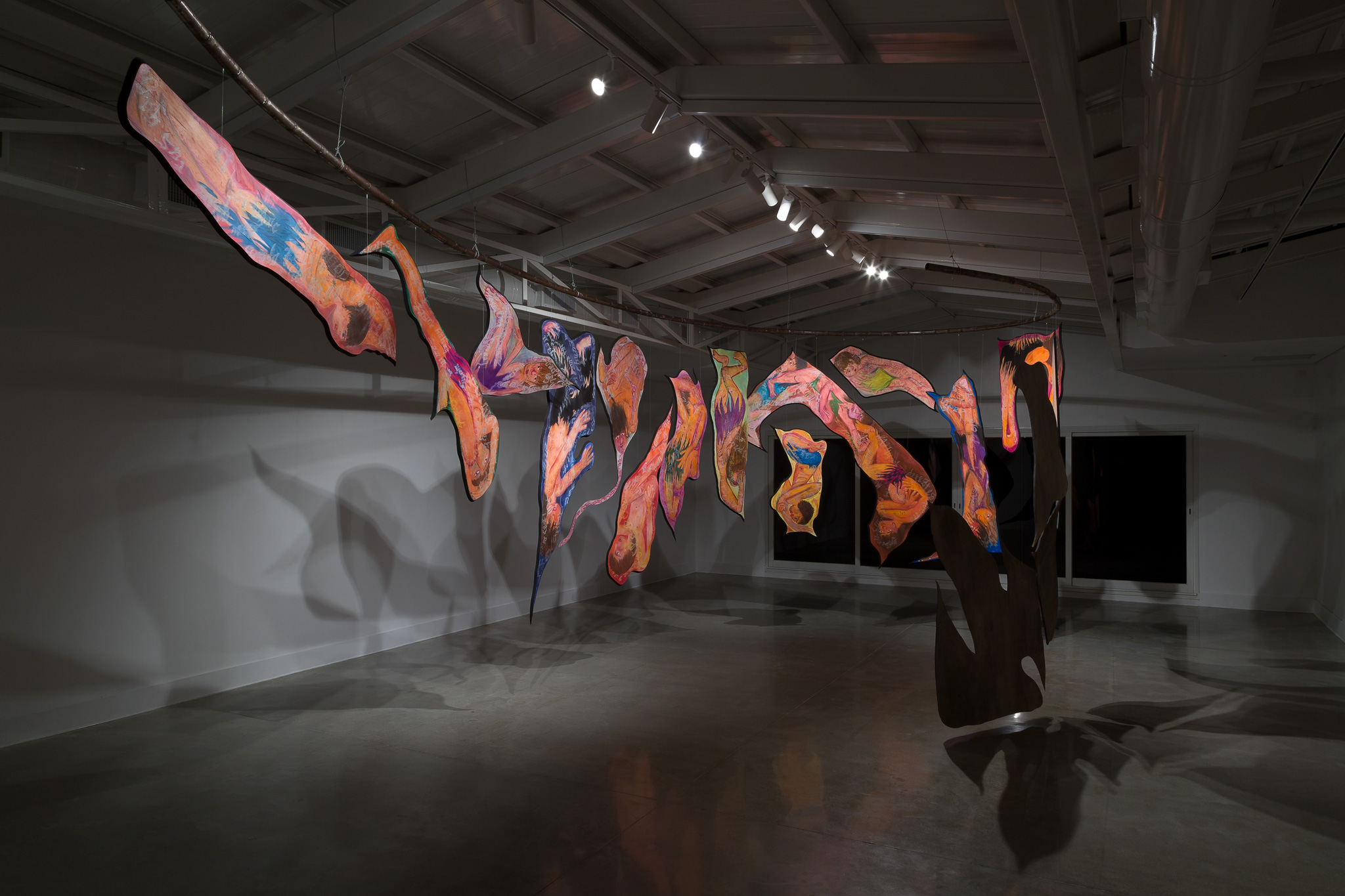 Each piece is suspended from a tubular structure that rotates in an elliptical shape within the room, creating a spatial dynamic in constant motion. The work establishes a dialogue between the materials and the space, inviting the viewer to experience the interaction of the rotating forms.