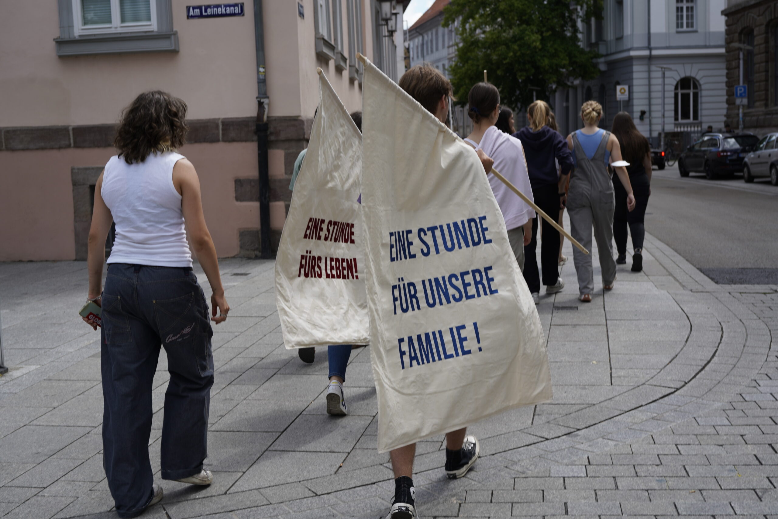 Several people carrying flags through the streets, showing slogans from the textile strikes of the 19th century in Germany.