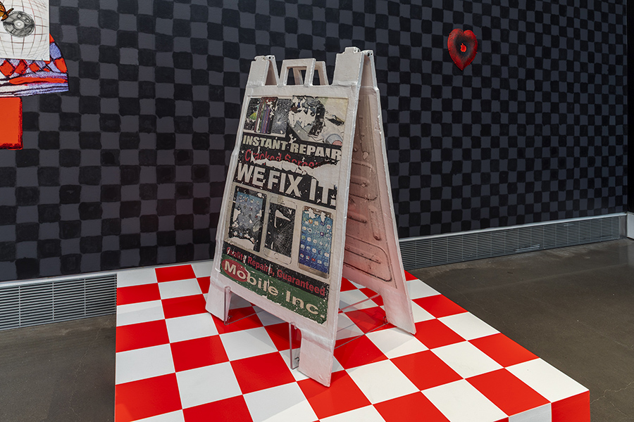 Art installation featuring a worn ceramic repair sign on a red and white checkered platform. Background has a dark checkerboard wall.